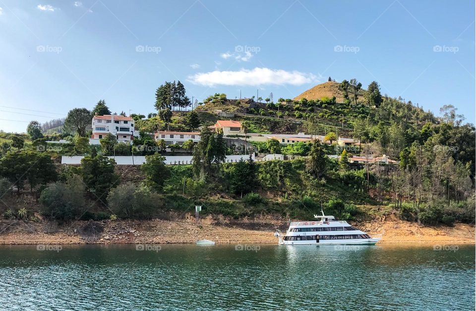 A boat is moored on the river below a hill scattered with villas and trees 