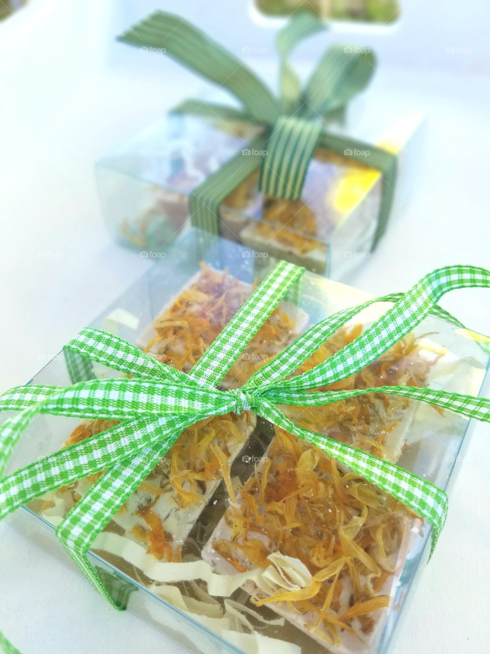 two gifts of artisan soap in clear boxes bound by patterned green ribbons