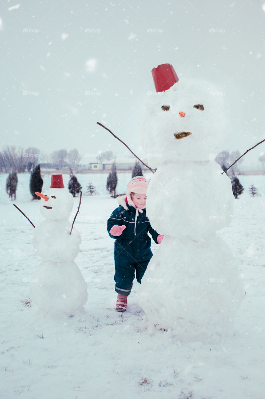 Little girl making a snowman, spending time outdoors, having fun in wintertime