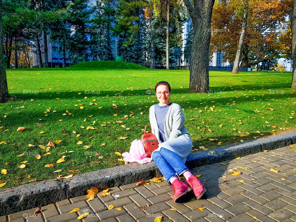 Young woman in town on the street near the autumn  park near the grass and yellow leaves.