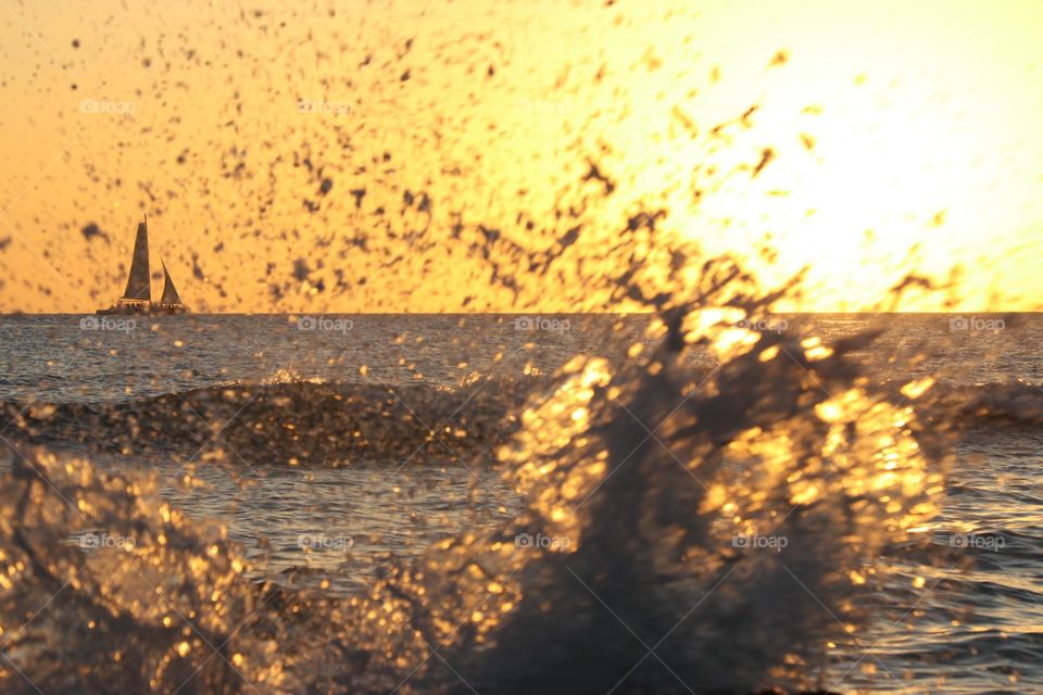 velero navegando al atardecer, detrás de olas rompiendo en la playa