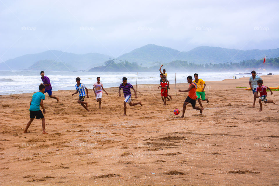 The beach soccer . A picture perfect click of local south goa boys playing soccer on the beach by the side of sea with a view of mountains 