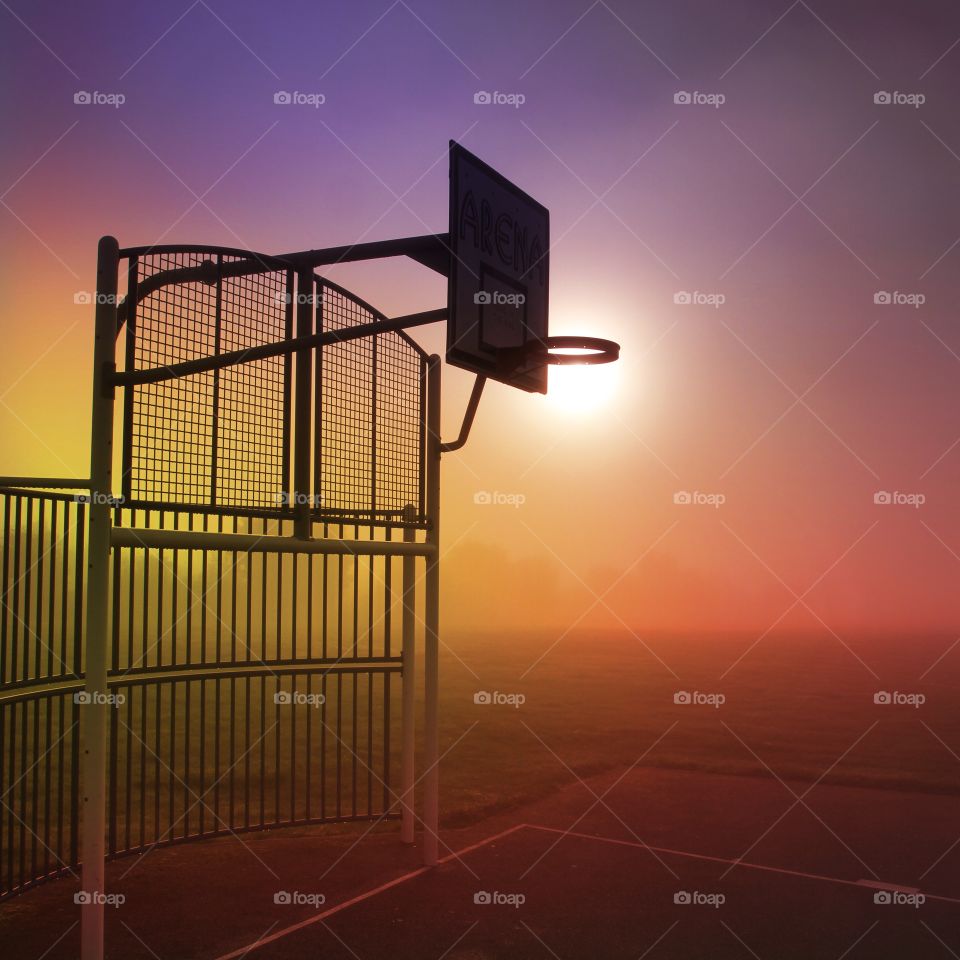 Early morning on an outdoor basketball court with a misty, colourful sky.