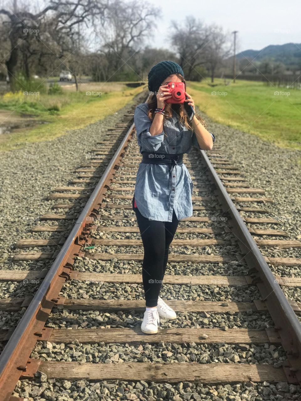 Traveling and discovering new places brings enormous happiness. It is possible to see a woman taking a picture with a Polaroid camera under a train track.
