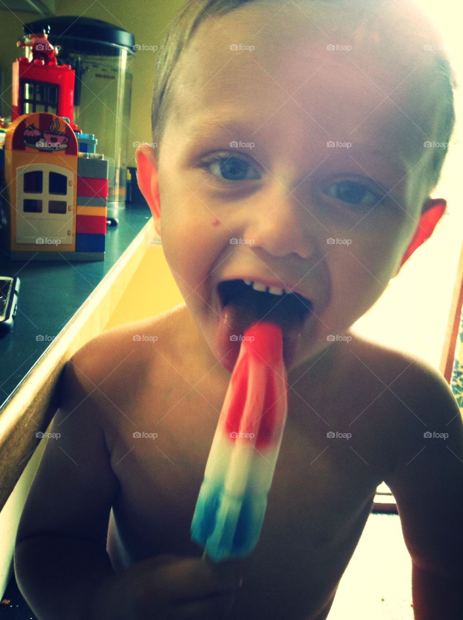 Cute boy licking popsicle ice at home