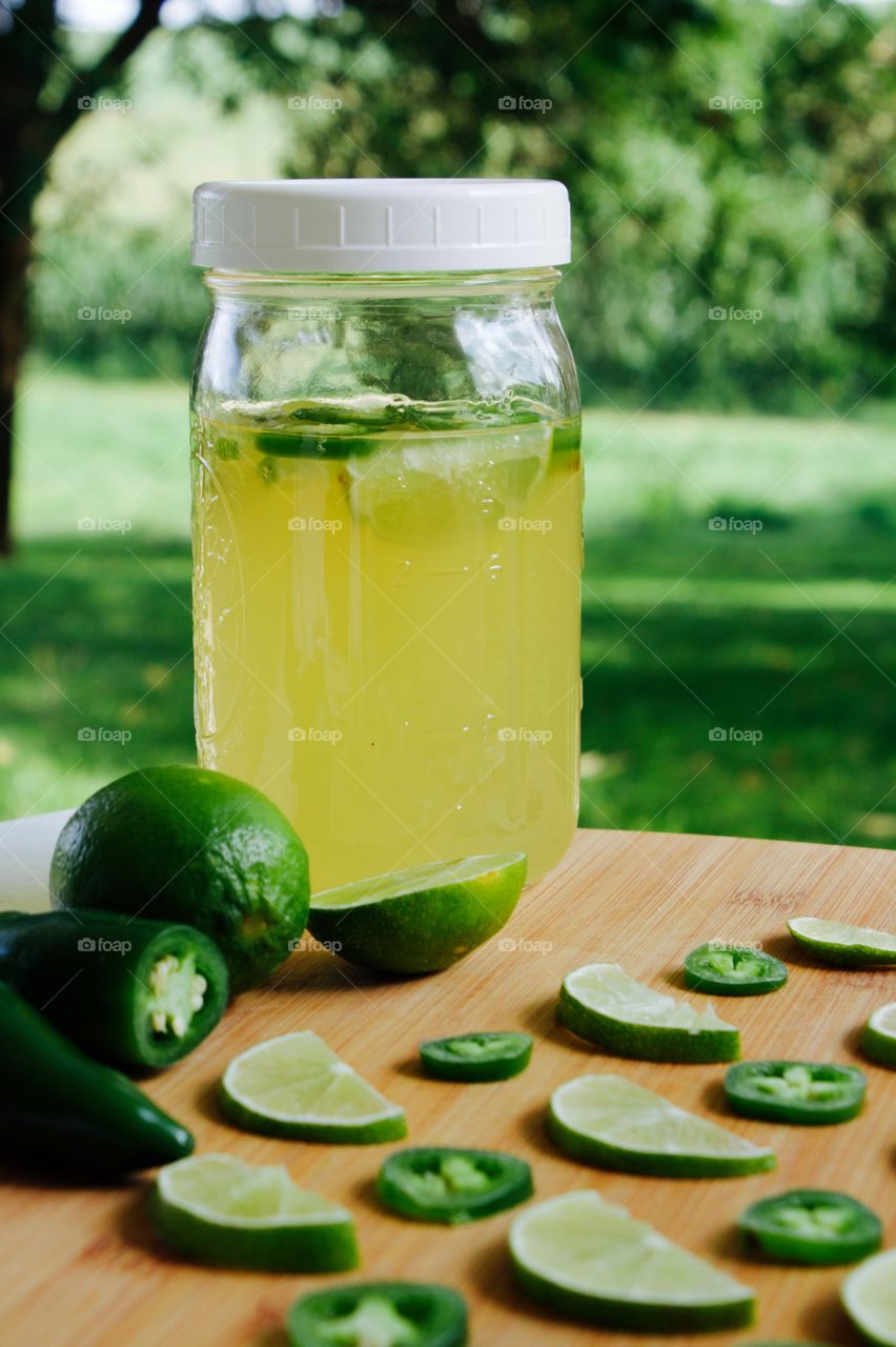 Refeshing lime-and-jalepeño-flavored kombucha, rebottled in a quart-size mason jar for a second ferment, with slices of lime and jalepeño on a bamboo cutting board, against a blurred outdoor background in summer