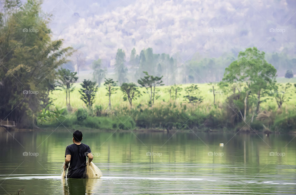 Man holding fishing nets walking in water Background blurred mountains and trees