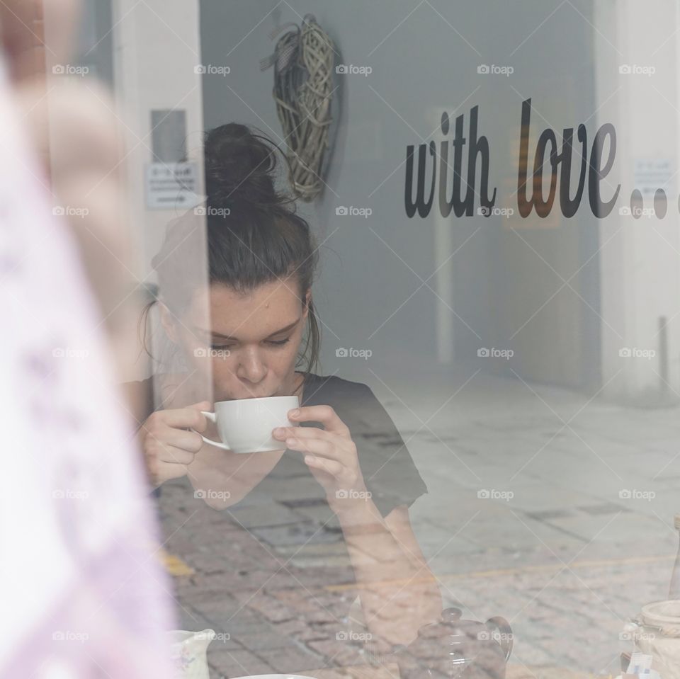 White coffee cup against a back painted wall of white ... photo taken through a shop window with the Manageress of the shop being my subject 