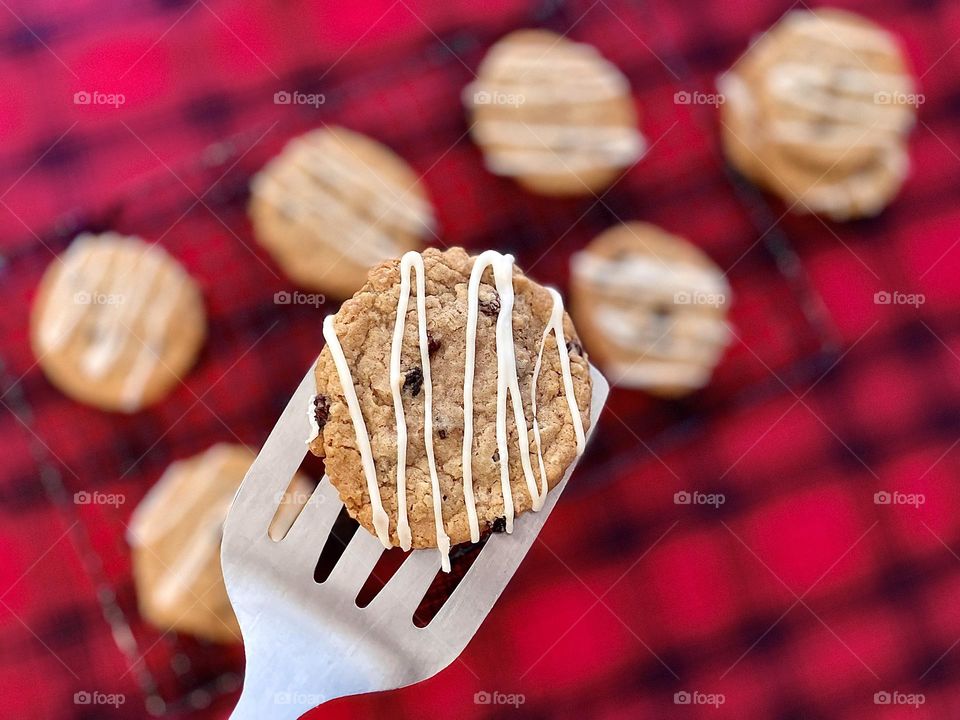 Freshly baked cookies on the cooking rack, using a spatula to move oatmeal cookies to a cooling rack, putting cookies on a cooling rack, delicious cookies made at home, icing drizzled on top of oatmeal raisin cookies, making cookies for the family 