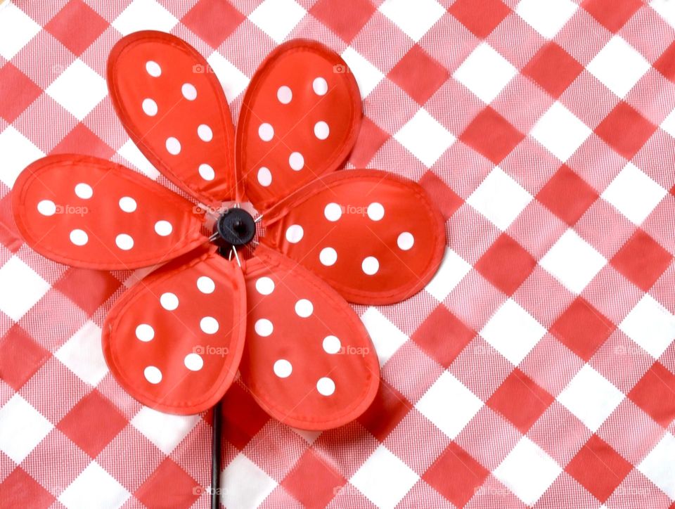 Red pinwheel with white polka dots on a red and white plaid tablecloth 