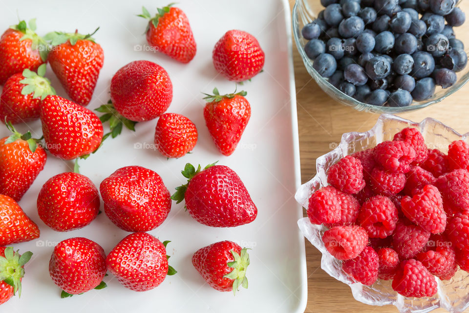 Delicious fresh healthy strawberries, blueberries and raspberries served in glass bowls and plate 