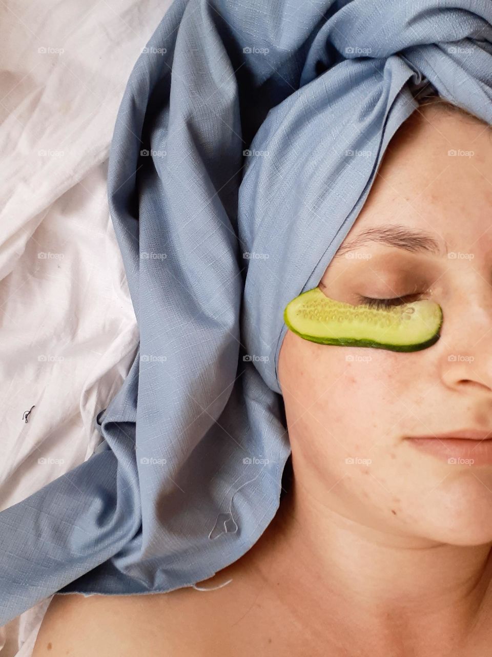 portrait of a white-skinned girl during home procedures, namely with a piece of cucumber under her eye