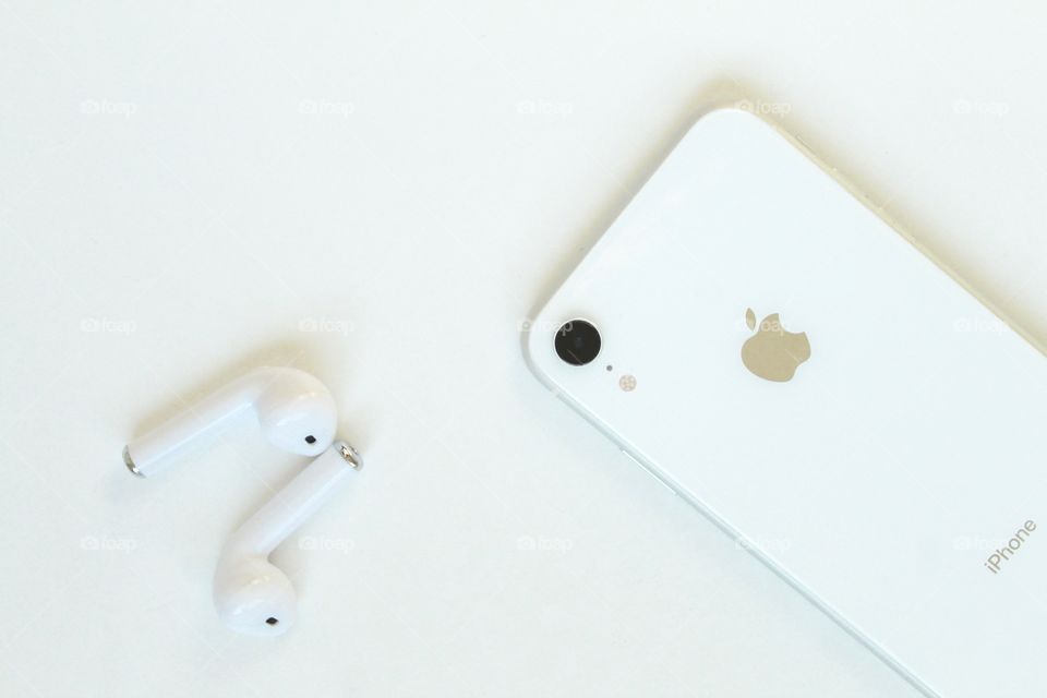 White cell phone and headphone on white desk.