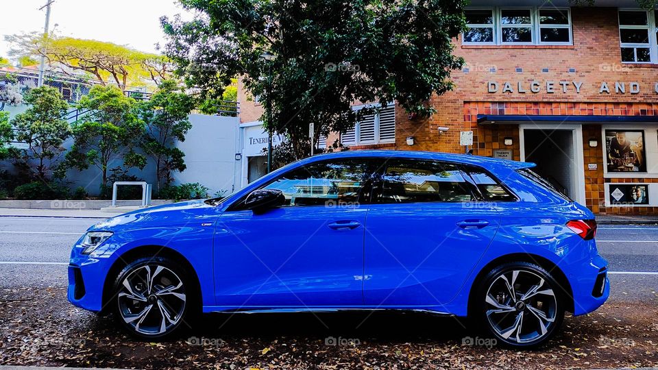 Bright blue luxury car parked in front of a brick building.