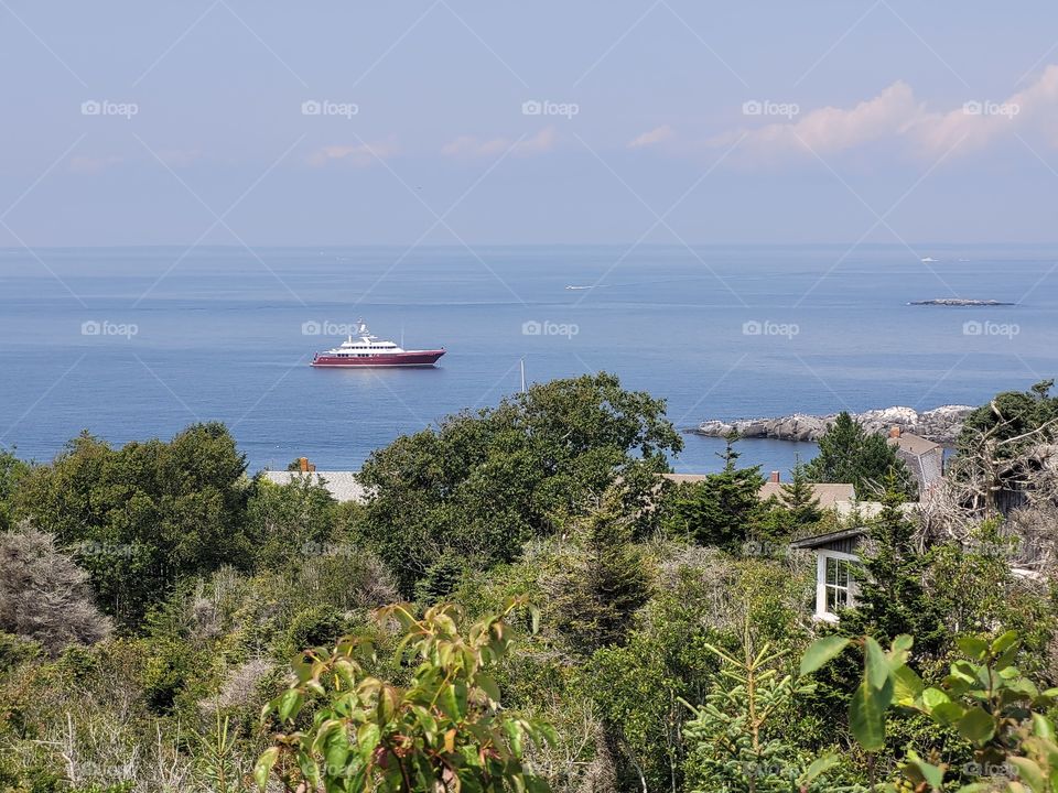 Looking out to sea from a wooden island in Maine. There is a red and white ship in the distance.