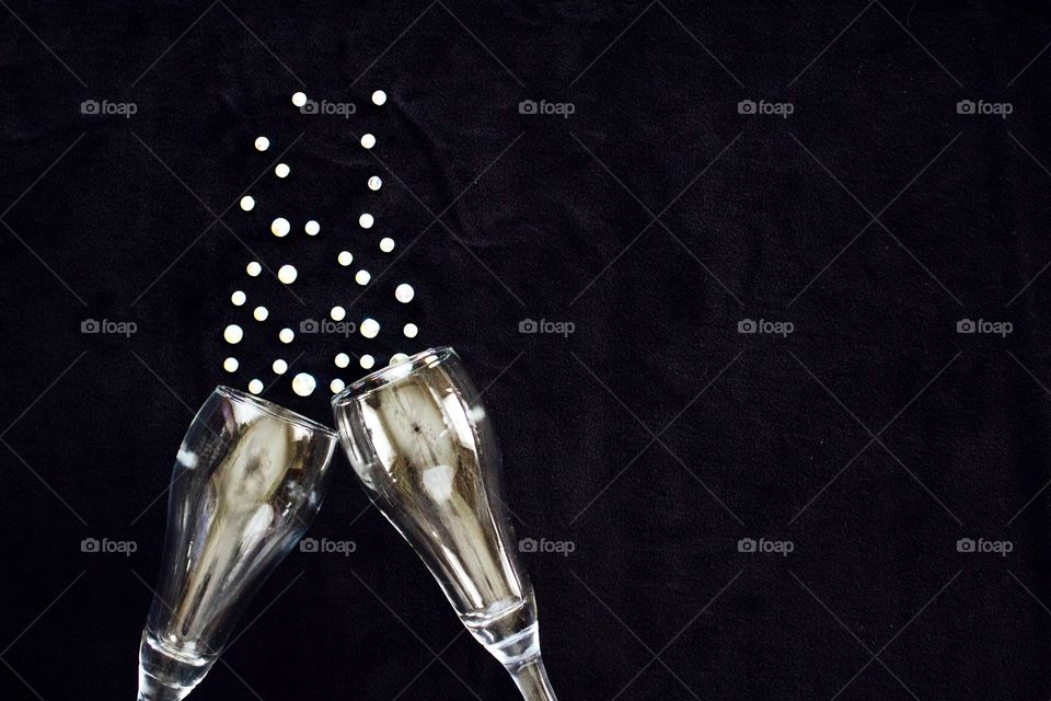 Flat lay of gleaming champagne glasses and  rhinestone bubbles on black background