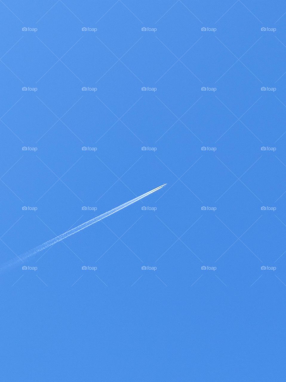 A simple photo of a clear blue sky with an airplane crossing it and leaving a white streak behind it