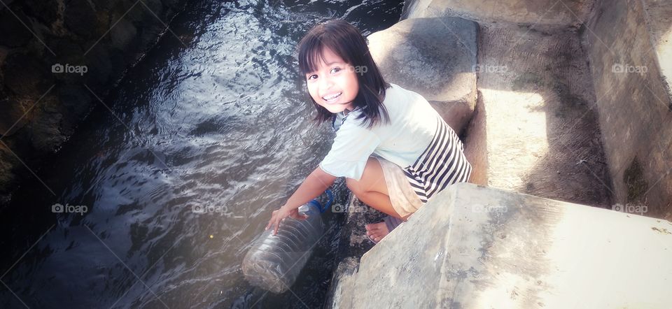 Sweet smile little girl is fetching water in the river
