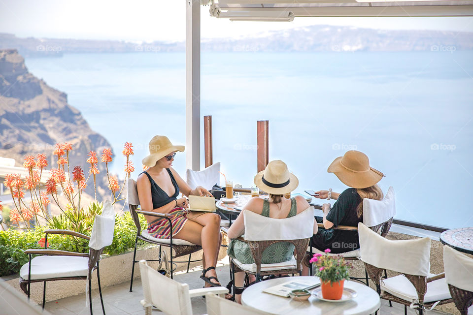 Three women on vacation sitting at an outdoor cafe in famous greek island Santorini. Travel destination in Greece, Europe.