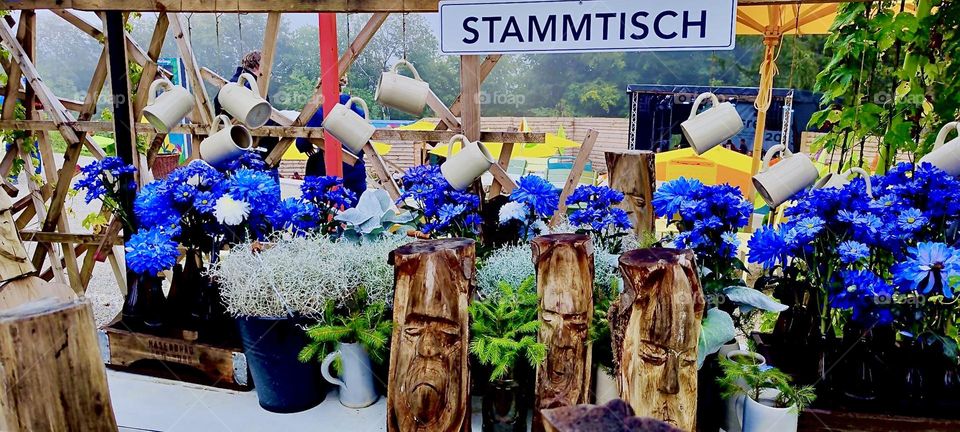 A whimsical presentation at the „Bayerische Landesgartenschau“, the „Bavaria State Garden Show“ in „Freyung“ is the „STAMMTISCH“, the „regular table“. Instead of drinking liquor these plants are watered from metal pitchers. 2023. Hypnotic Productions