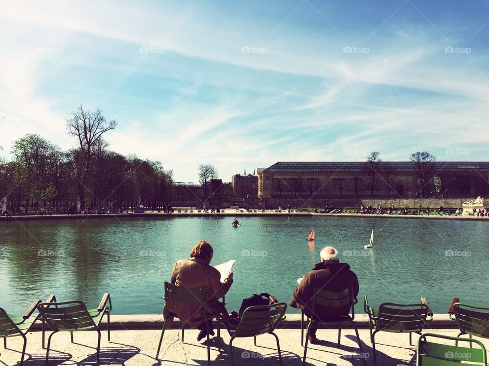 Two elderly people sitting on a bench in a park in Paris, taken from behind