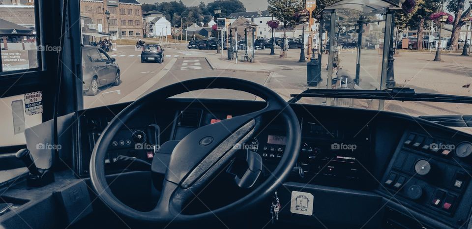 A beautiful view of the city street with a stop from the cab of a passenger bus with a large steering wheel, close-up side view. Road trip concept.