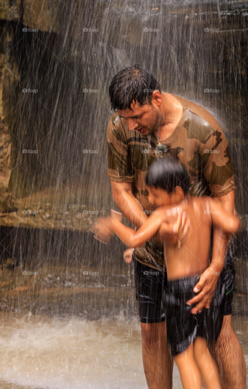 Father holding his son in rain enjoying and protecting