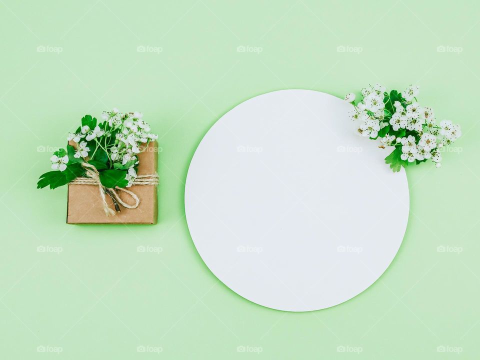 One cardboard small box tied with jute thread with apple flowers and a round empty callout lie on a pastel green background, flat lay close-up.