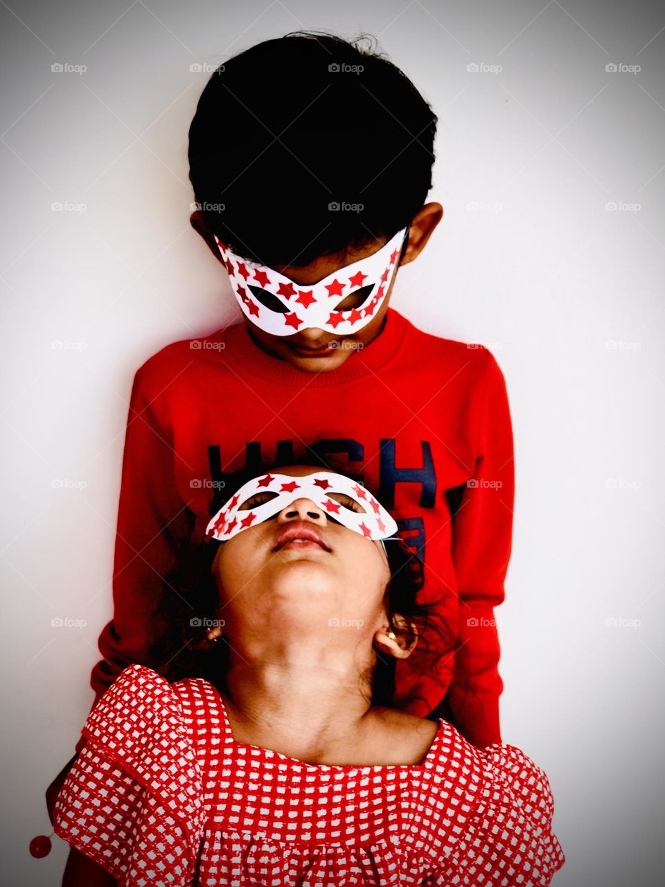 Kids wear eye mask and looking at each other and they both wear red colour dress.