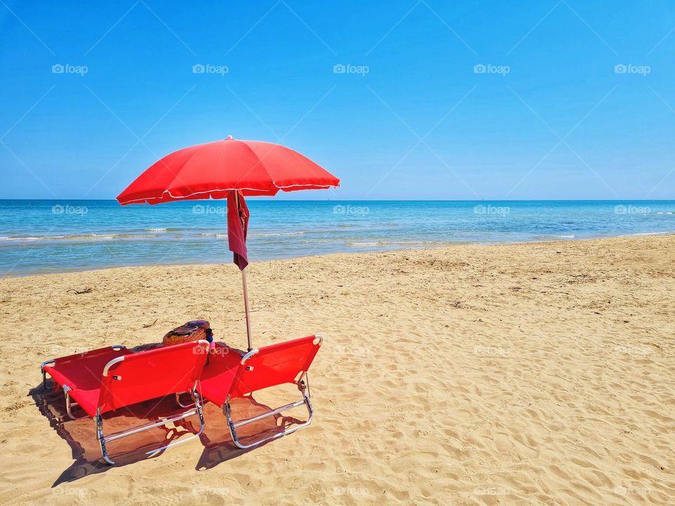 beach umbrella and red deck chairs on a deserted sunny beach