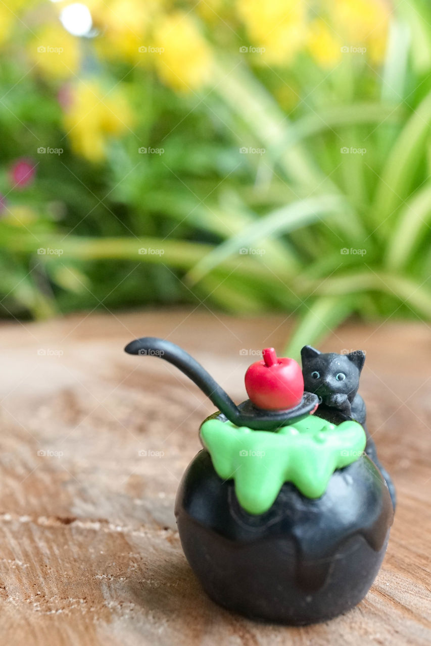 Halloween black cat. Miniature of Halloween black cat is making magic potion with poison red apple on top. Abstract background of flower garden with natural light. Soft focus on the cat's face.
