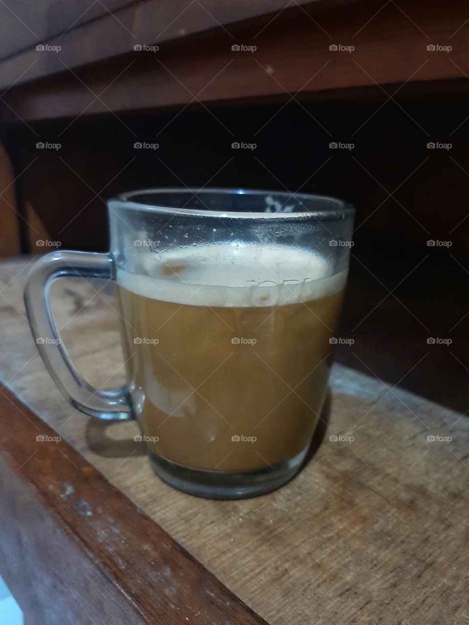 A glass of coffee on the small wooden table.