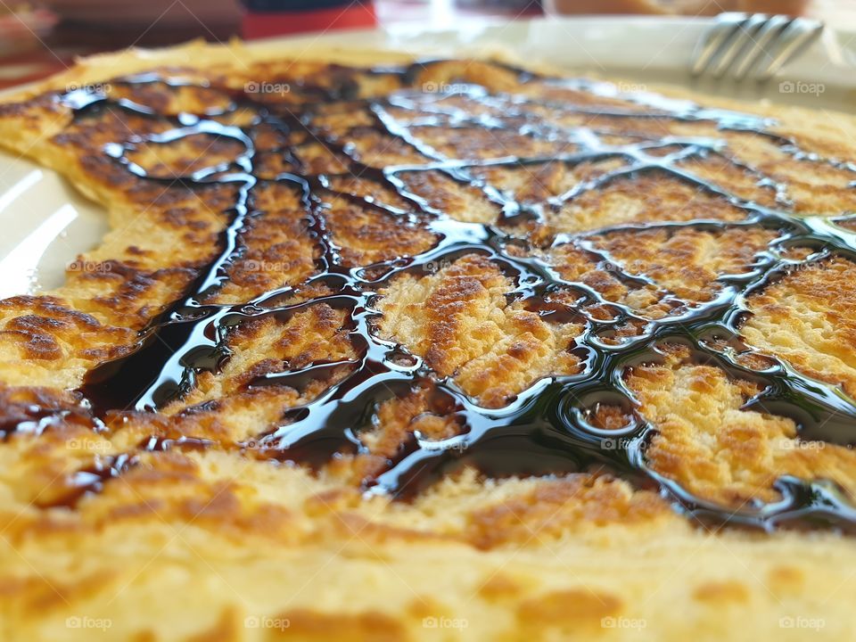 A portrait of a delicious pancake covered in belgian black candi syrup ready to be rolled up and eaten.