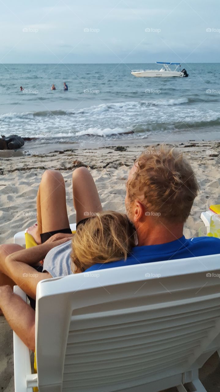 A couple shares a beach chair.