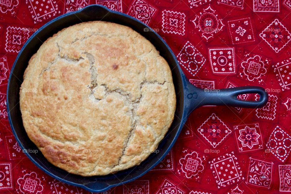 Flat lay of freshly baked sourdough cornbread in a cast iron skillet on a red bandana-print tablecloth