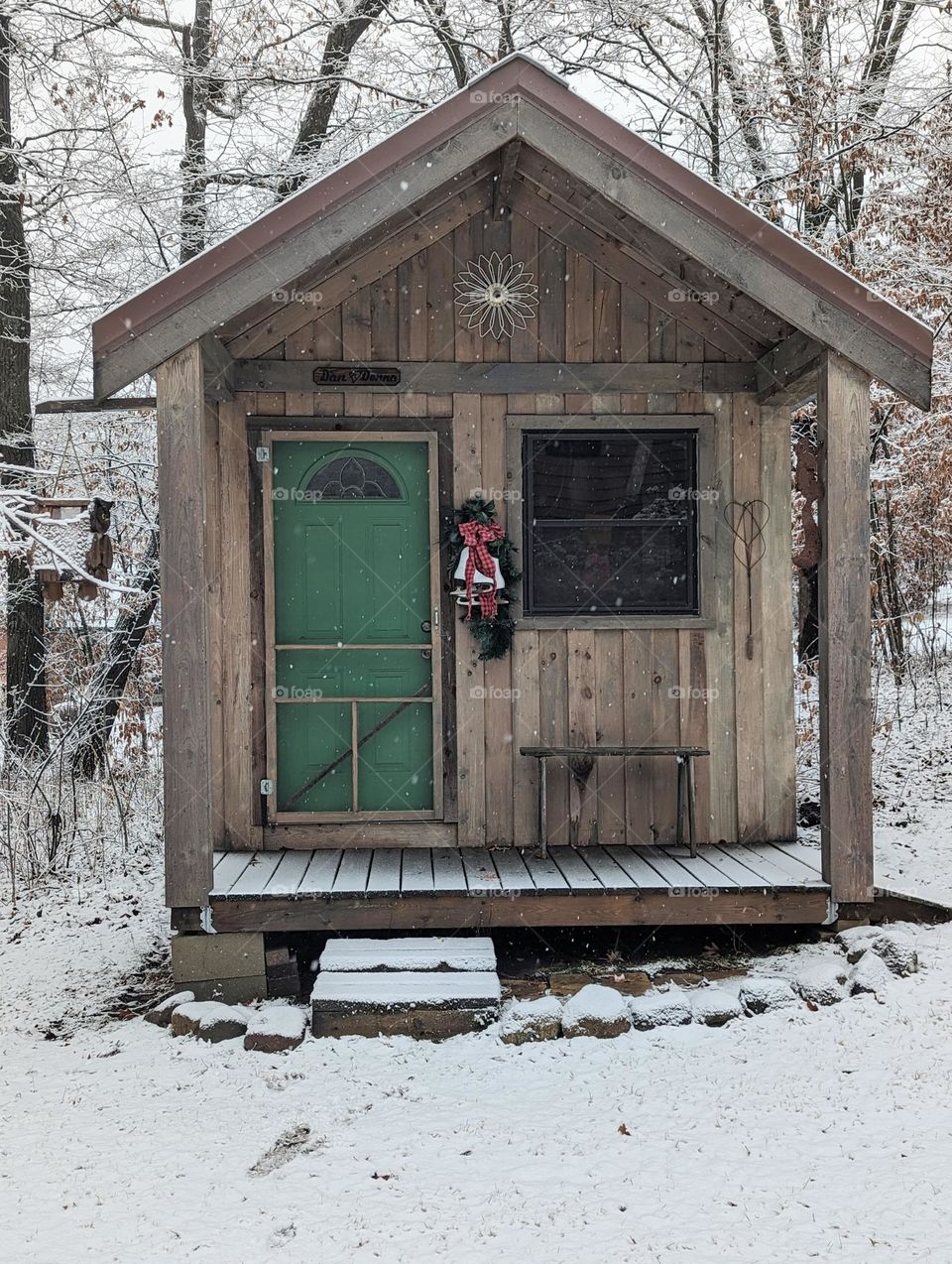 rustic winter garden shed in frosty fresh snow, wooden outdoor shed in winter with green door and Christmas decorations