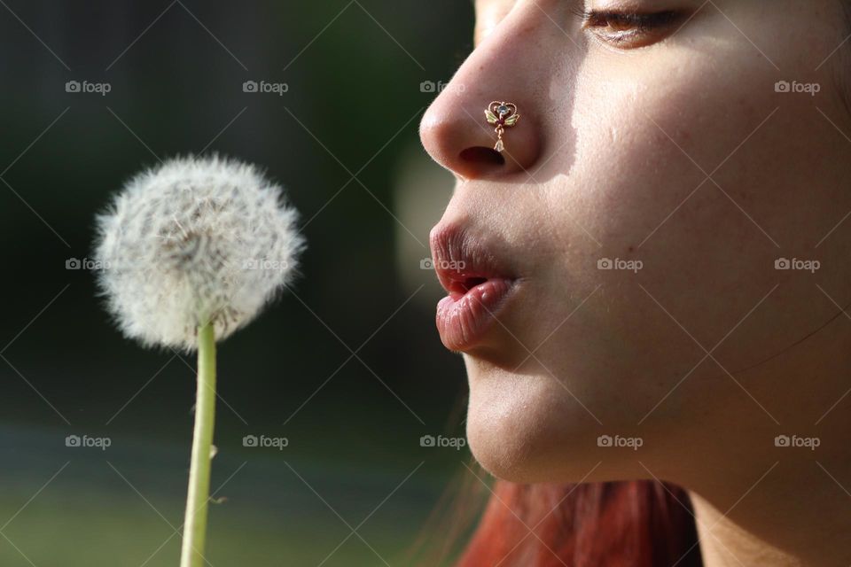 Nose piercing jewellery on a young woman with dandelion