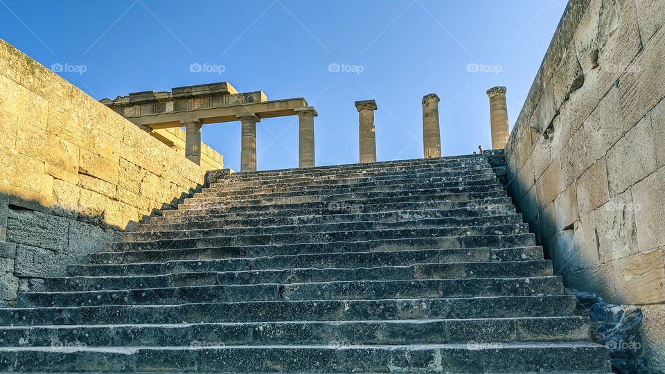 A beautiful view of the stone right hand with rectangular stone steps up to the ruined ancient temple of Athena in Greece on the island of Rhodes, close-up from below.