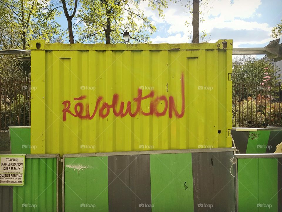 Light green Construction container tagged with word Revolution in French in red paint with trees and sky behind