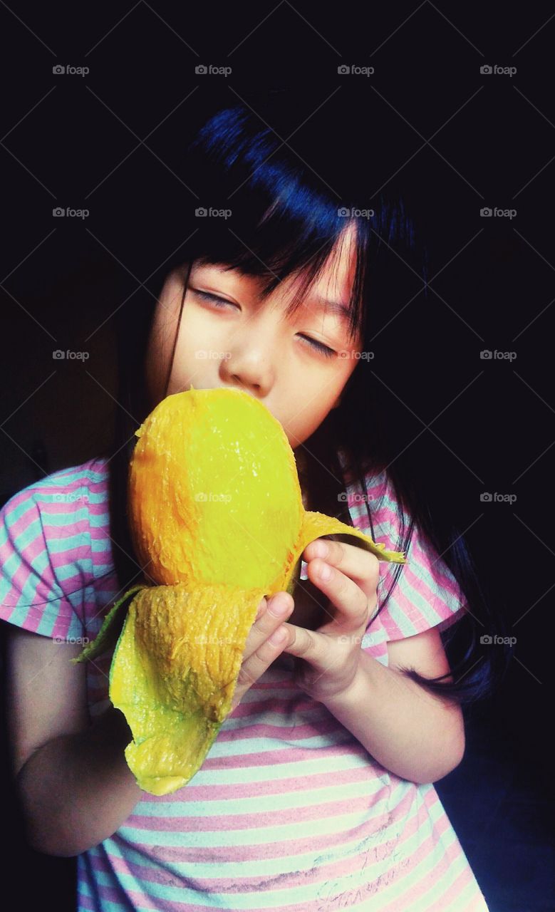 Little Asian girl eating mango