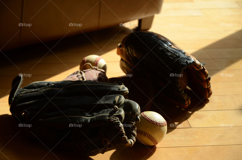 Baseballs and gloves lay the livingroom floor near the back porch of a residential home.