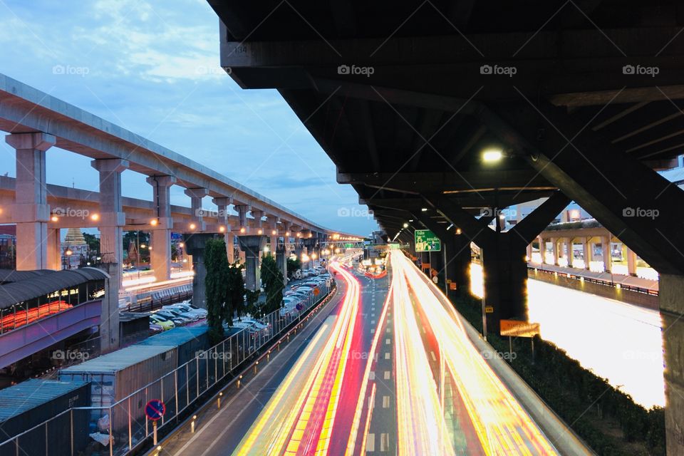 Long light tails of cars on the road under highways 