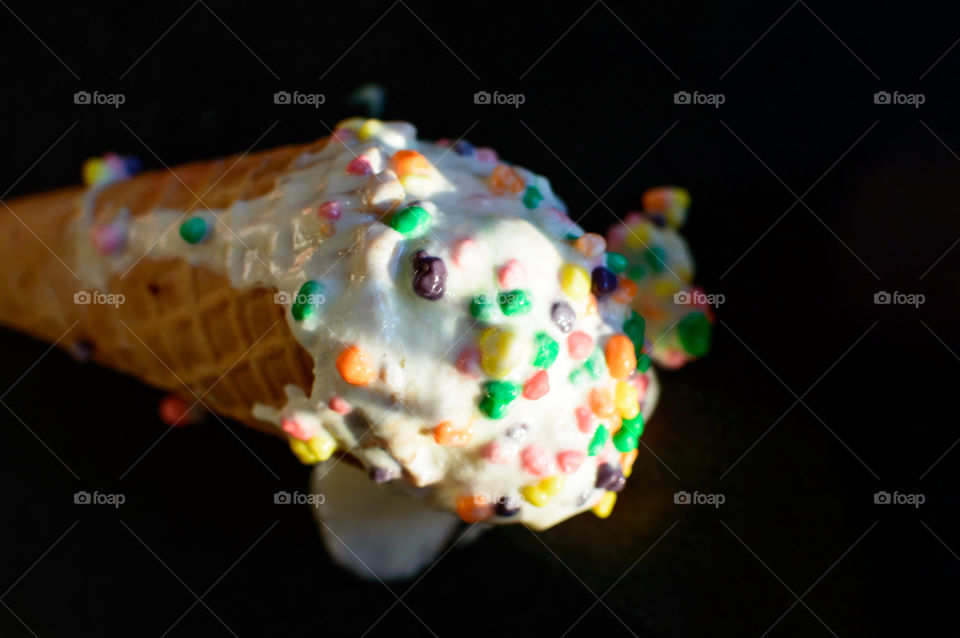 White Vanilla ice cream scoops with colorful sprinkles in a sugar waffle cone melting in sunlight on counter isolated studio shot black background fun gourmet photography with room for copy