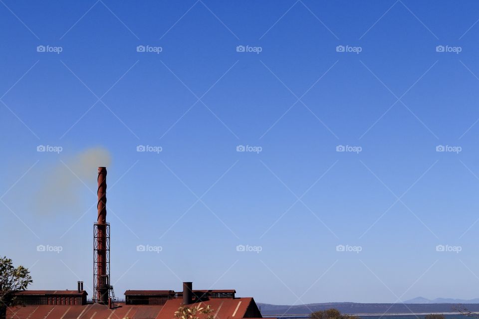 Steel mining smelter tower blowing plume of smoke into vivid blue sky 