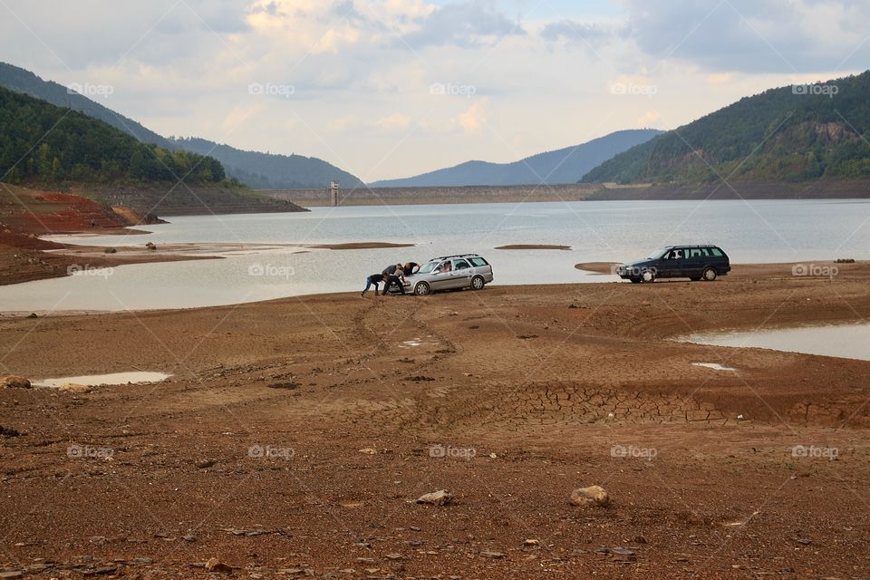 Friends pushed a mired car in the mud after the rain on the shore of the dam
