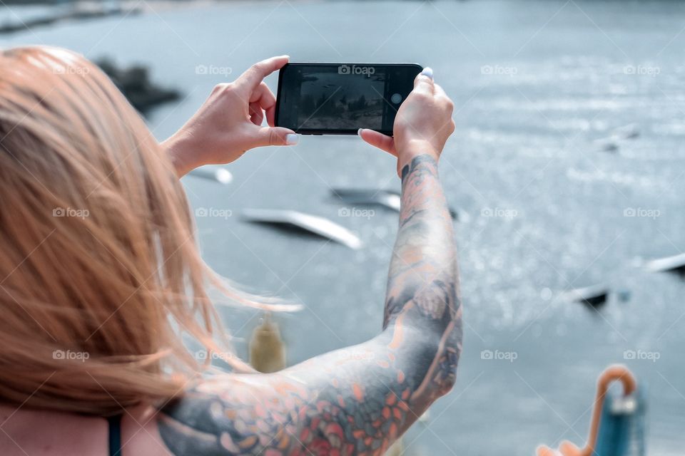 Beautiful tattoo young lady make a photo of the lake on her smartphone 