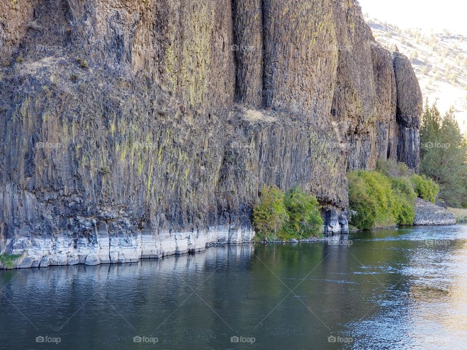 The beautiful Crooked River with fall colored bushes on its banks flows through a canyon formed from andesite and basalt flows on a nice autumn evening in Central Oregon. 