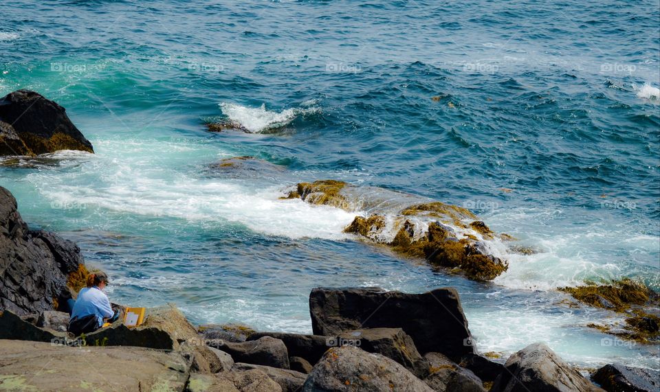 Woman sitting on the rocky edge of the sea looking out at the ocean in Maine.