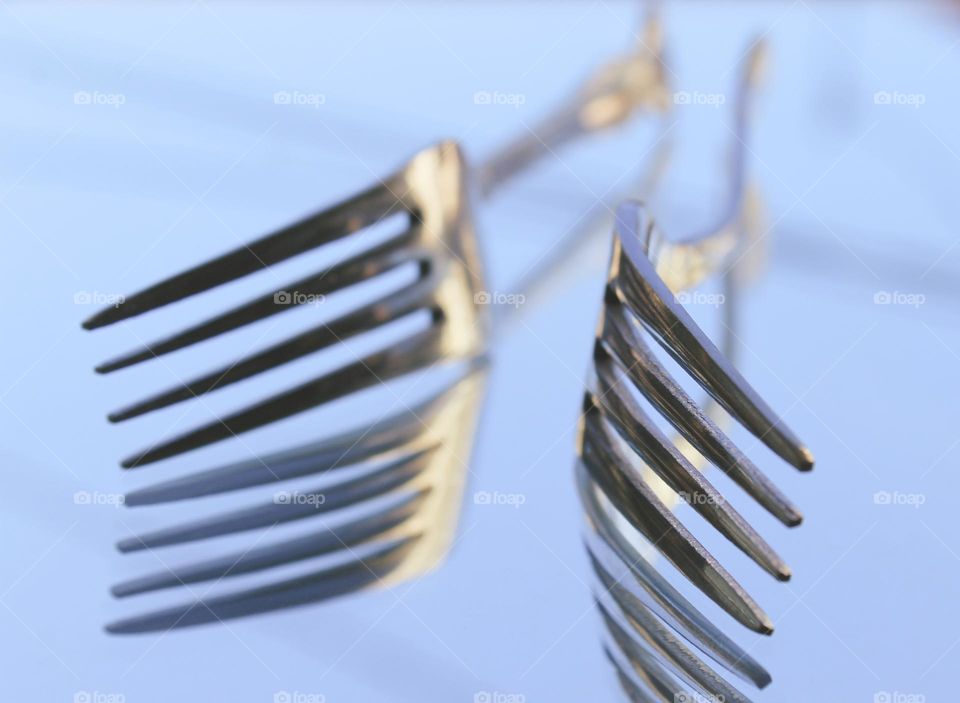 Close up of two metal forks are reflected in a mirror.  A fork is a cutlery or kitchen tool