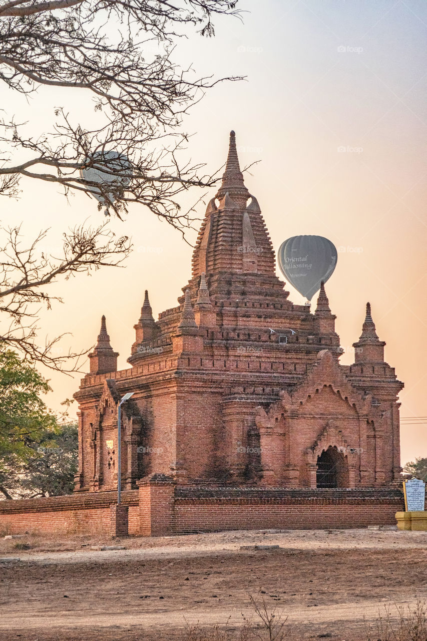 Beautiful sunrise in Bagan with an ancient temple in the foreground and the famous hot air balloons in the background
